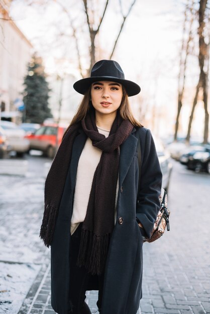 Mujer joven elegante en sombrero y capa con la bufanda en la calle