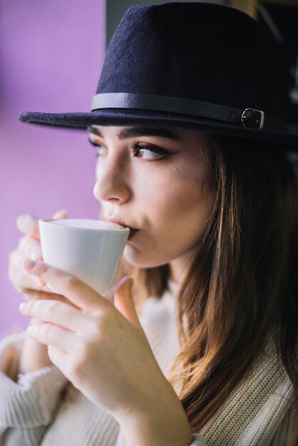 Mujer joven elegante en sombrero con la taza de bebida