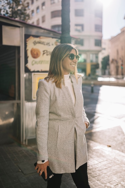 Mujer joven elegante sonriente con las gafas de sol y smartphone en la calle