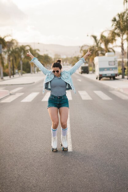 Mujer joven elegante sonriente que equilibra el patín de ruedas que lleva en el camino