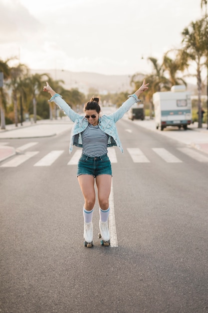 Mujer joven elegante sonriente que equilibra el patín de ruedas que lleva en el camino