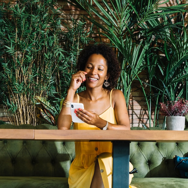 Foto gratuita mujer joven elegante sonriente que mira el teléfono móvil en el restaurante