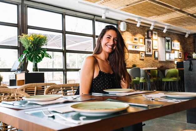 Mujer joven elegante sonriente que se sienta en el restaurante