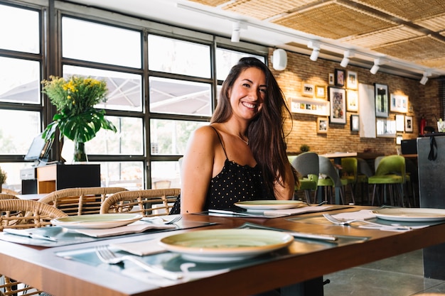 Mujer joven elegante sonriente que se sienta en el restaurante