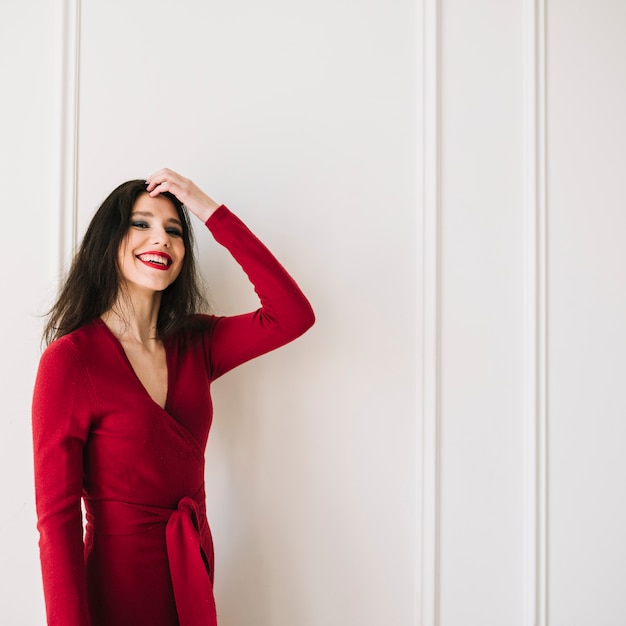 Mujer joven elegante sonriente en el vestido rojo que sostiene el pelo en sitio