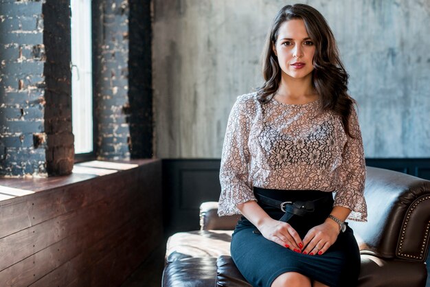 Mujer joven elegante en la tapa floral que se sienta en el sofá