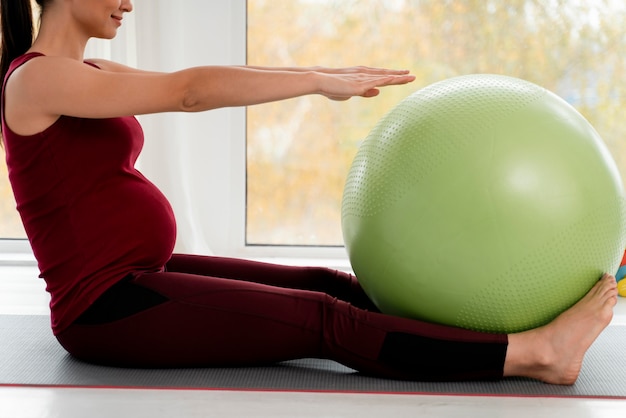 Mujer joven embarazada haciendo ejercicio con pelota verde fitness