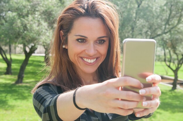 Mujer joven emocionada alegre que toma el selfie en parque