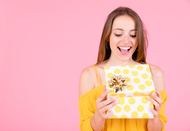 Mujer joven emocionada que abre la caja de regalo amarilla del lunar con el arco de oro