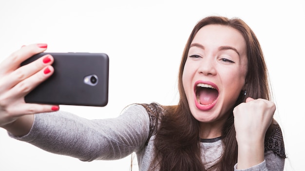 Mujer joven emocionada que hace la foto del selfie a través del teléfono móvil