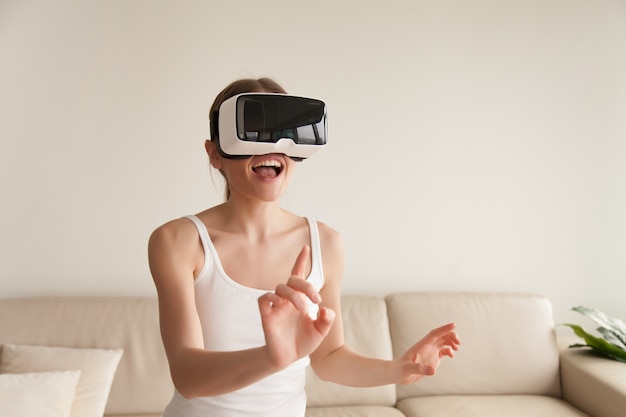 Mujer joven emocionada que lleva las auriculares de VR que tocan realidad virtual