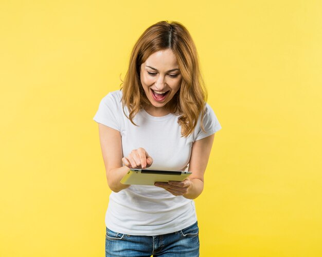 Mujer joven emocionada que señala el dedo en la tableta digital contra el contexto amarillo