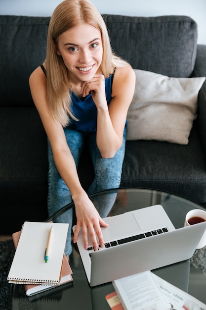 Mujer joven encantadora alegre que usa la computadora portátil en casa