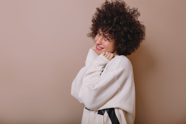 Mujer joven encantadora inspirada riendo en suéter lindo que presenta en beige