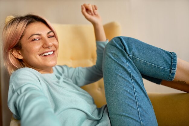 Mujer joven encantadora oprimista positiva con anillo en la nariz riendo, relajándose en casa el fin de semana