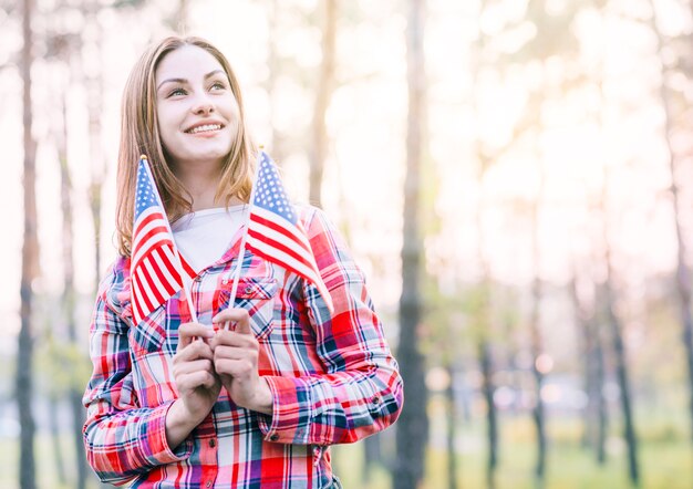 Mujer joven encantadora que sostiene pequeñas banderas americanas