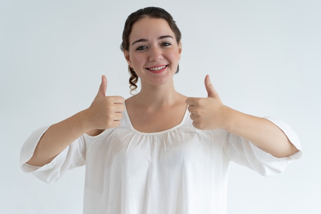 Mujer joven encantadora sonriente que muestra los pulgares para arriba