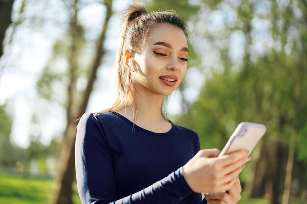 Mujer joven enciende música para correr en su teléfono inteligente al aire libre