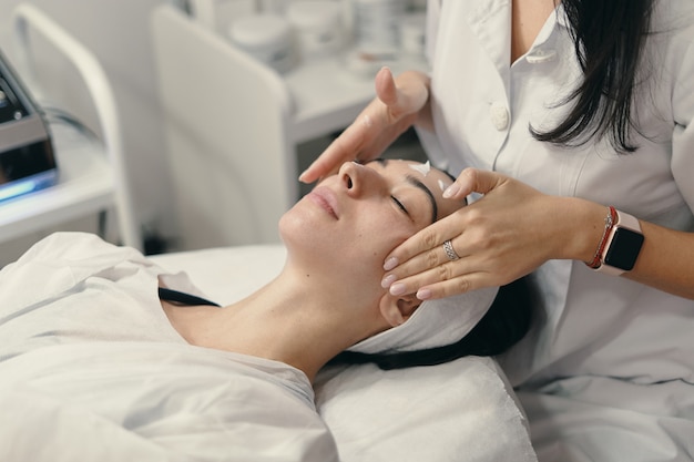 Mujer joven se encuentra con los ojos cerrados, cosmetóloga haciendo procedimiento