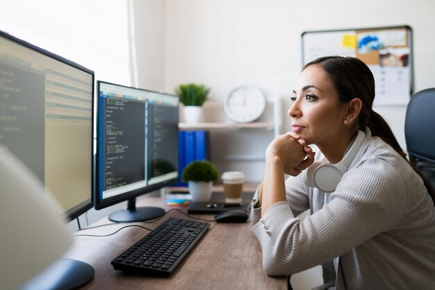 Mujer joven enfocada leyendo y codificando en la computadora. Vista lateral de un programador independiente que trabaja desde casa