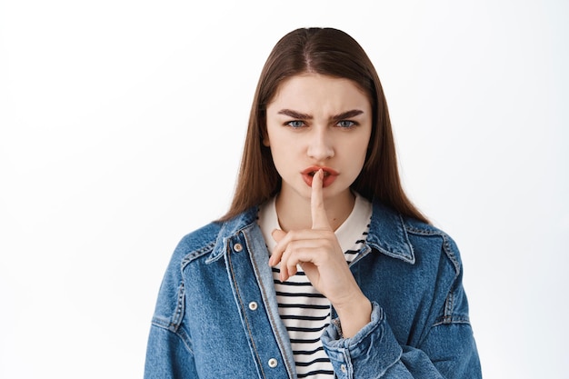 Foto gratuita mujer joven enojada callando, frunciendo el ceño y haciendo shhh gesto de silencio con el dedo en los labios, signo tabú, decir que se calle, prohibir hablar, de pie sobre fondo blanco