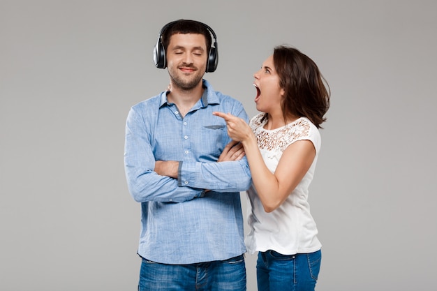 Foto gratuita mujer joven enojada con hombre en auriculares sobre pared gris