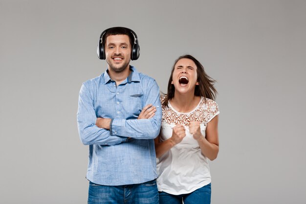 Mujer joven enojada con hombre en auriculares sobre pared gris