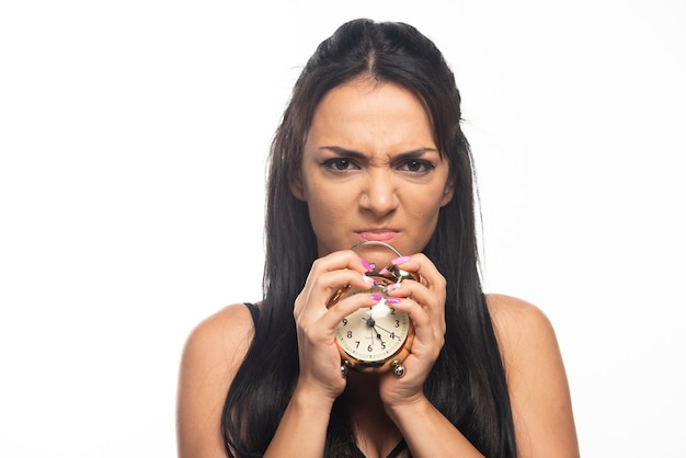 Foto gratuita mujer joven enojada sosteniendo un reloj de alarma en la pared blanca