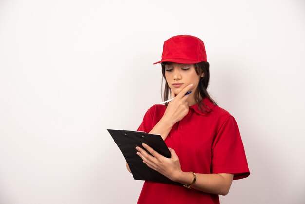 Mujer joven de entrega en uniforme rojo con portapapeles sobre fondo blanco.