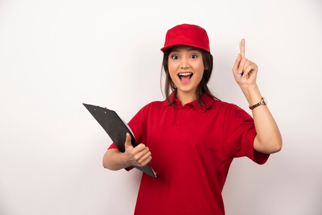 Mujer joven de entrega en uniforme rojo con portapapeles sobre fondo blanco.