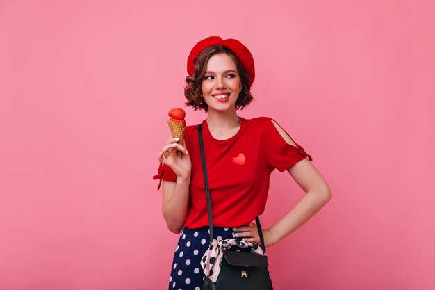 Mujer joven entusiasta en ropa de moda comiendo helado. Foto interior de dama despreocupada sonriente con postre.