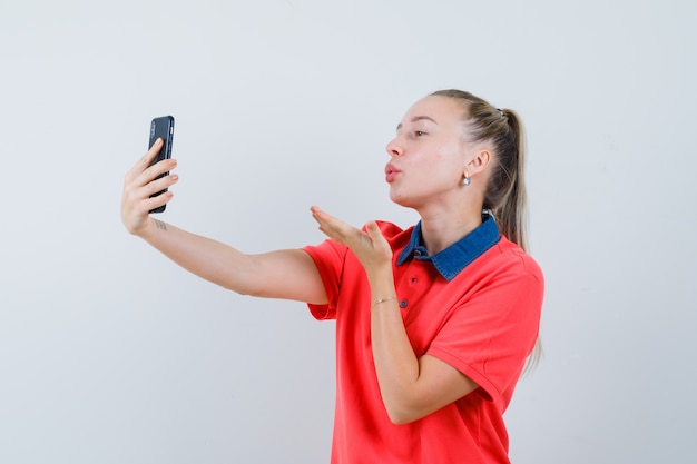 Mujer joven enviando beso de aire mientras toma selfie en camiseta