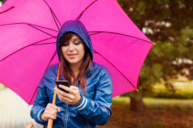 Mujer joven enviando mensajes de texto en el teléfono móvil bajo la lluvia