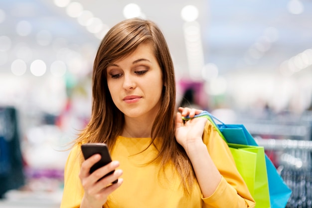 Mujer joven enviando mensajes de texto por teléfono móvil en la tienda