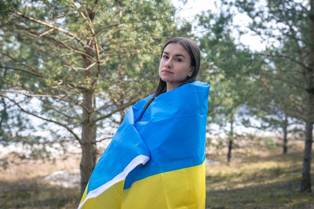 Una mujer joven envuelta en la bandera de ucrania en un fondo borroso