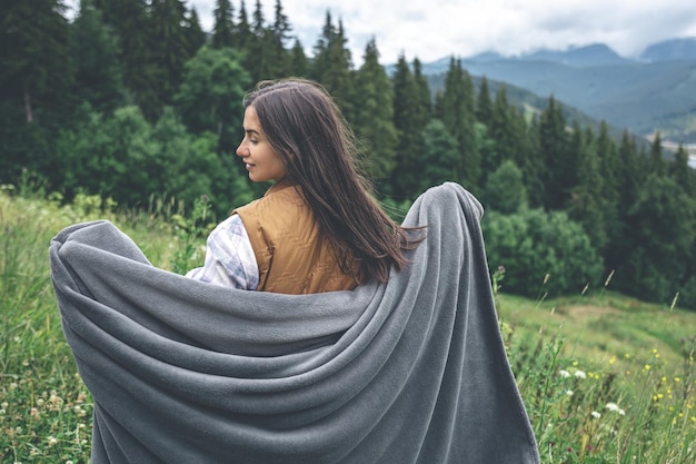 Una mujer joven envuelta en una manta en las montañas.
