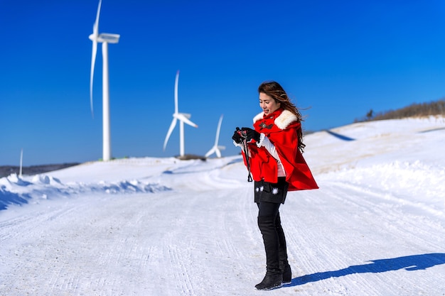 La mujer joven es una felicidad con la cámara en invierno del cielo y la carretera de invierno con nieve y vestido rojo