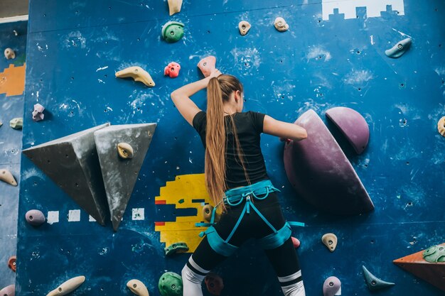 Mujer joven escalando un muro de escalada alto, interior, artificial