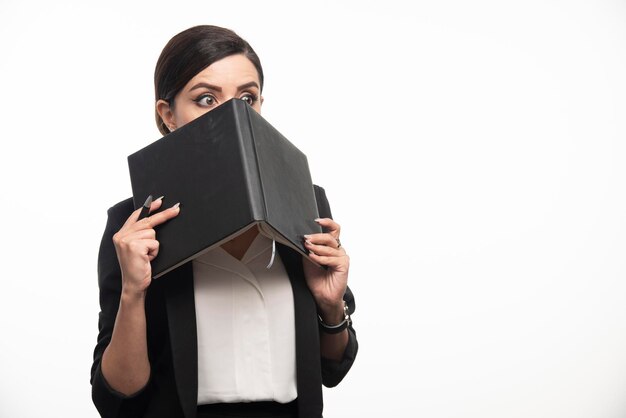 Mujer joven escondida detrás de un libro sobre fondo blanco. Foto de alta calidad
