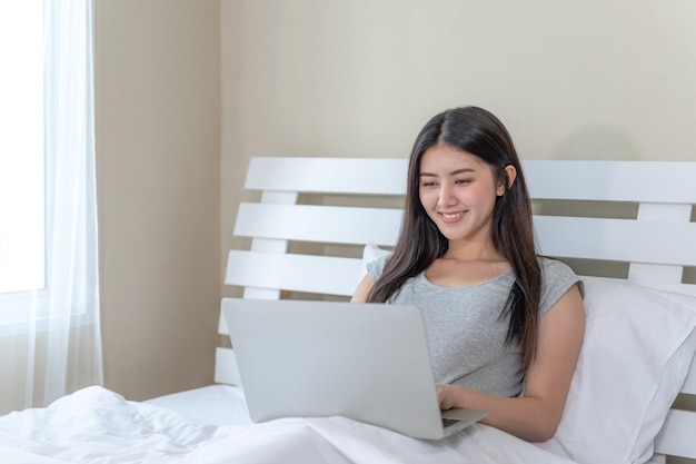 Mujer joven escribiendo en la computadora portátil en el dormitorio