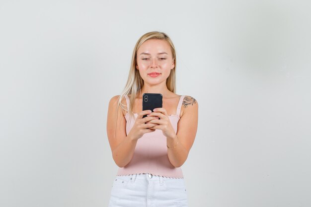 Mujer joven escribiendo en smartphone y sonriendo en camiseta