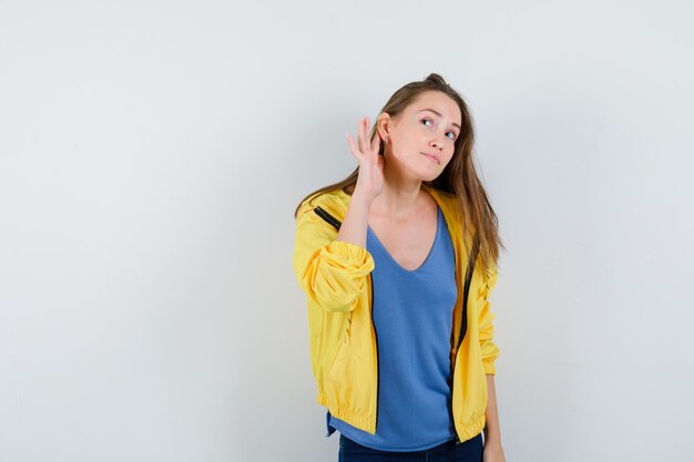 Mujer joven escuchando una conversación privada en camiseta, chaqueta y con curiosidad. vista frontal.