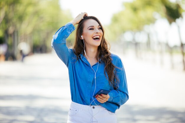 Mujer joven escuchando música con auriculares en la calle de verano