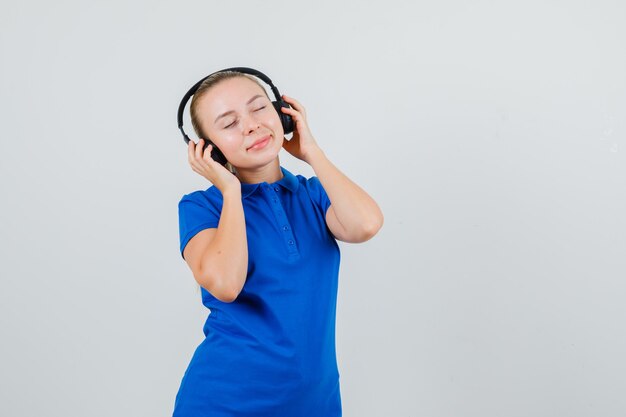 Mujer joven escuchando música con auriculares en camiseta azul