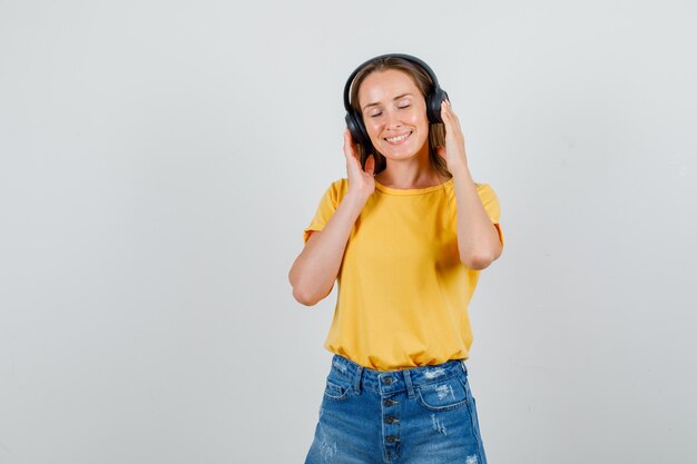 Mujer joven escuchando música con auriculares en camiseta, pantalones cortos y aspecto relajado. vista frontal.