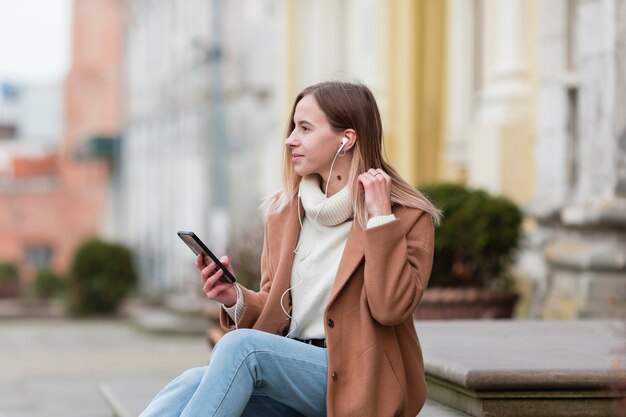 Mujer joven escuchando música en auriculares en la ciudad
