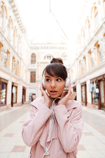 Foto gratuita mujer joven escuchando música con auriculares y mirando al aire libre