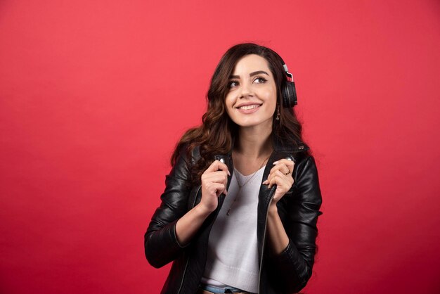 Mujer joven escuchando música en auriculares y posando sobre un fondo rojo. Foto de alta calidad