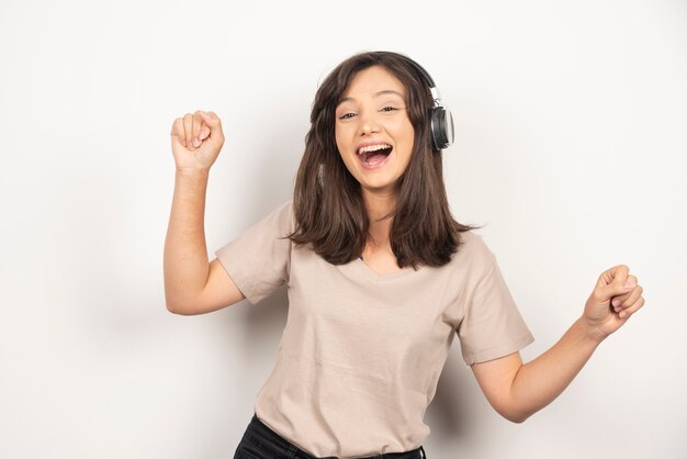 Mujer joven escuchando música en auriculares sobre fondo blanco.