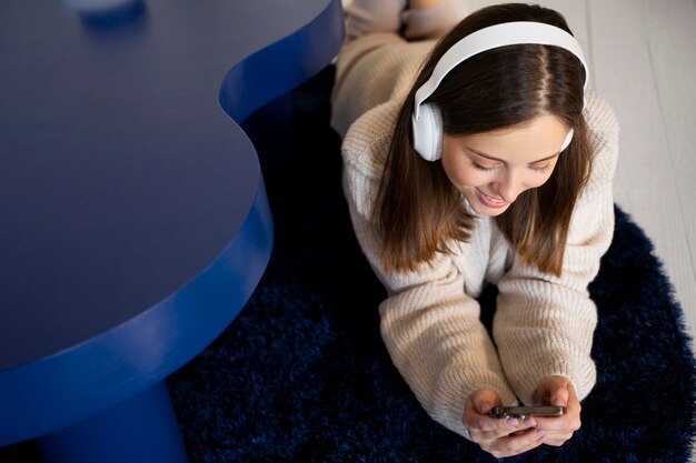 Mujer joven escuchando música con su teléfono inteligente mientras está acostado en el suelo